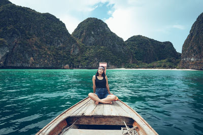 Full length of woman sitting on boat in sea against mountains