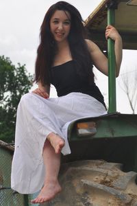 Portrait of smiling young woman sitting against sky