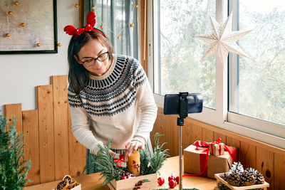 Female florist blogger making winter ikebana with pine branches, candle and christmas decorations