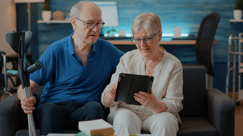 Senior man with woman using digital tablet while sitting on sofa