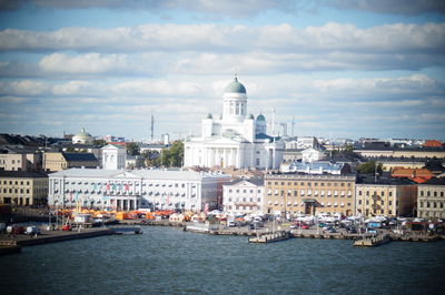 Buildings at waterfront against cloudy sky