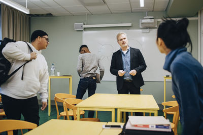 Male teacher talking to female student standing in classroom