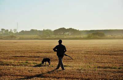 Rear view of man with dog on agriculture field against sky