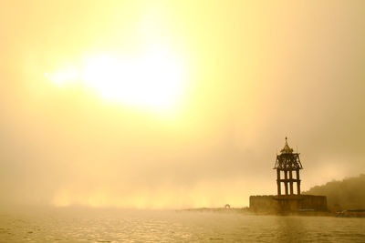 Lighthouse by sea against sky during sunset