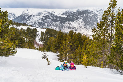 Mother and daughter lying down on a snow smiling and looking at camera. winter ski holidays, andorra