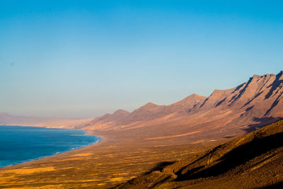 Scenic view of sea and mountains against clear blue sky