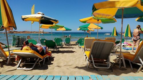 People and lounge chairs with umbrella at beach during sunny day