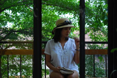 Woman wearing hat standing against trees