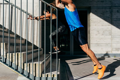 Side view of cropped unrecognizable fit couple in sportswear jumping on stone steps on street during workout in summer