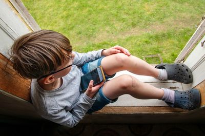 High angle view of boy sitting on window sill