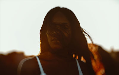 Close-up portrait of young woman with tousled hair against clear sky