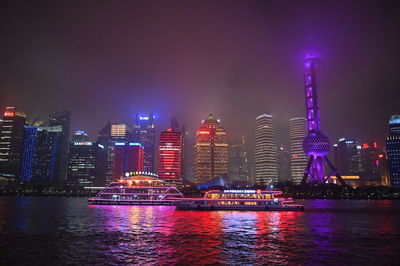 Illuminated buildings by river against sky in city at night