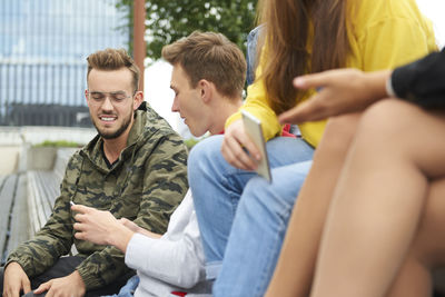 Happy friends talking while sitting at park in city