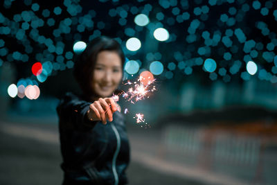 Smiling woman holding lit sparkler at night