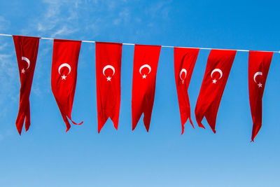 Low angle view of red flags hanging against blue sky