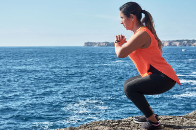 Side view of woman exercising on rock against sea