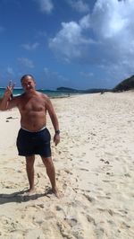 Full length of shirtless man standing on beach against sky