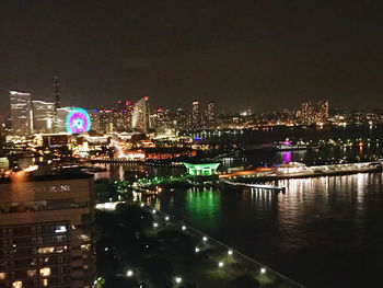 Illuminated city by river against sky at night