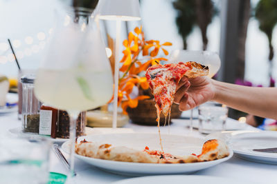 Woman hand holding pizza in a plate on dinner table.