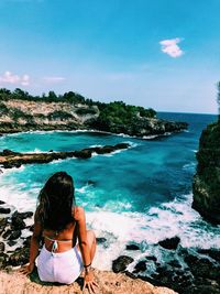 Rear view of woman sitting on rock at beach