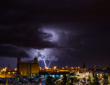 Buildings in city against dramatic sky at night