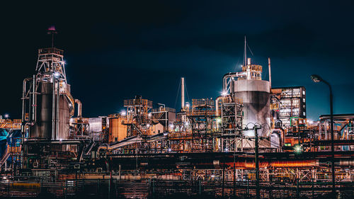 Illuminated factory against sky at night