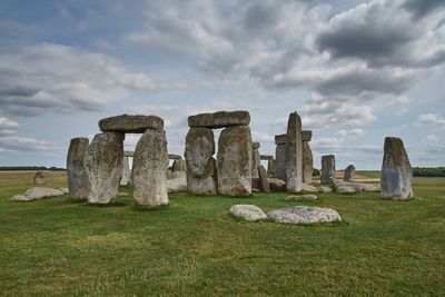 Stone structure in field against cloudy sky