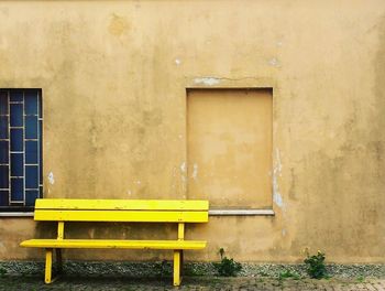 Empty yellow bench against wall