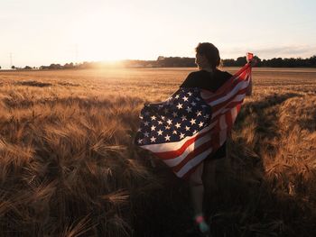 Rear view of woman on field against sky during sunset