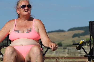 Young woman wearing sunglasses sitting on land against sky