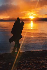 Silhouette man piggybacking woman at beach against sky during sunset