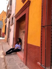 Young woman sitting against door of building