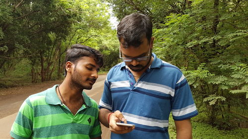 Young man looking at friend using phone on road in forest