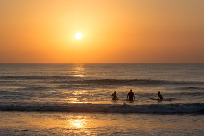 Silhouette people on sea against sky during sunset