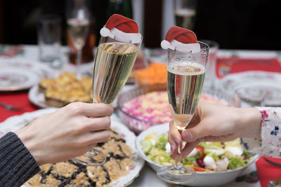 Cropped hands of friends toasting champagne flutes with santa hats at table