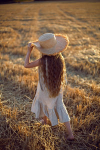 Girl child with long hair walking across the field wearing a hat with long hair during sunset