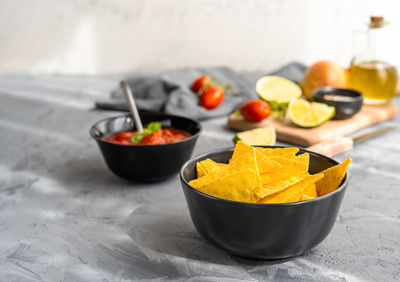 Traditional mexican nachos tortillas in black bowl with tomato dip and basic ingredients aside