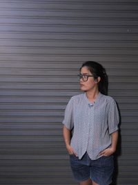 Young woman wearing sunglasses standing against wall