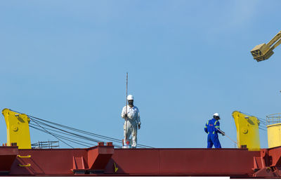 Low angle view of people working against clear blue sky