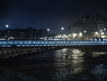 Illuminated bridge over river by buildings in city at night