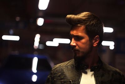 Young man wearing jacket looking away in illuminated parking lot