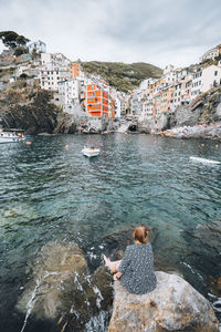 Young woman sitting on rock overlooking cove of famous italian village