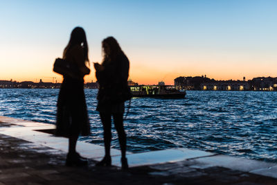 Silhouette women standing on promenade against sky during sunset