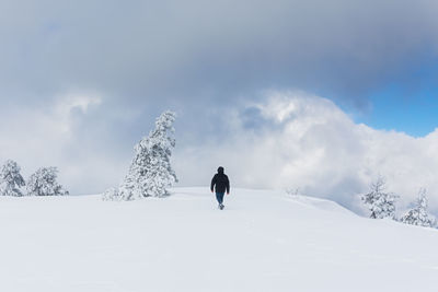 Rear view of man walking on snow covered field against sky