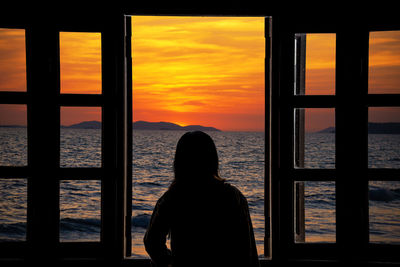 Rear view of silhouette woman looking at sea against sky during sunset