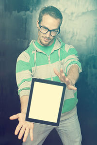 Portrait of young man showing digital tablet while standing against old wall