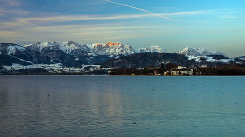 Scenic view of sea by snowcapped mountains against sky