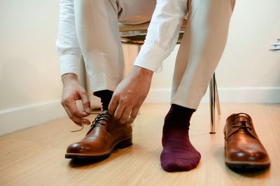 Low section of man tying shoelaces on hardwood floor at home