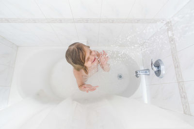 High angle view of girl with eyes closed enjoying shower in bathtub at home