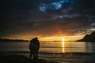 Couple embracing at beach against cloudy sky during sunset